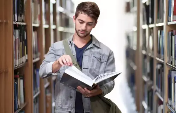 Um estuddante na Irlanda olhando um livro entre os corredores da biblioteca.