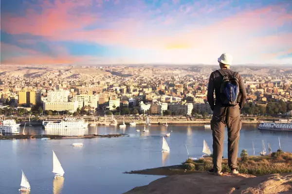 Prédios e casas da cidade, rio e barcos, e homem observando tudo, em Aswan