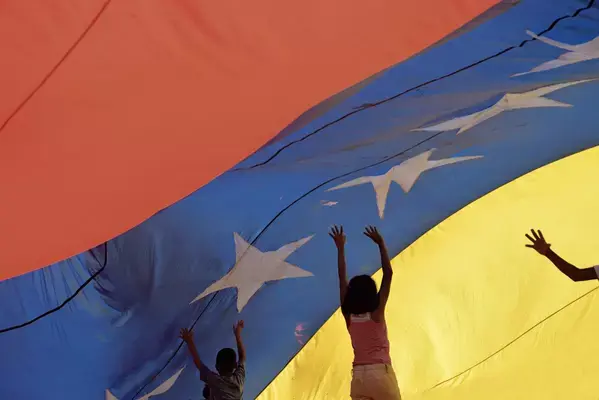 Crianças embaixo de uma grande bandeira da Venezuela