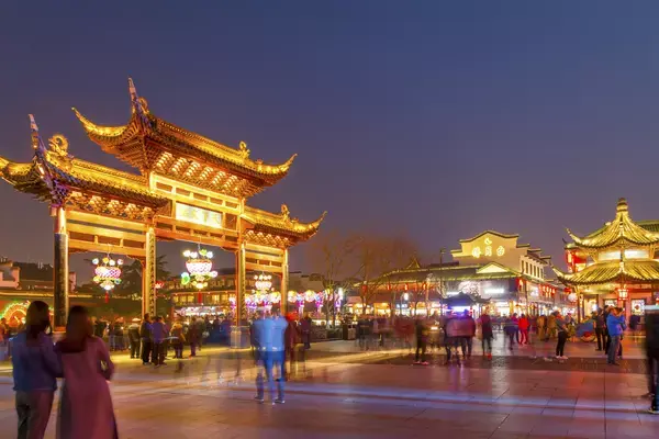 Visão noturna de uma cidade na China, com pessoas borradas passando.