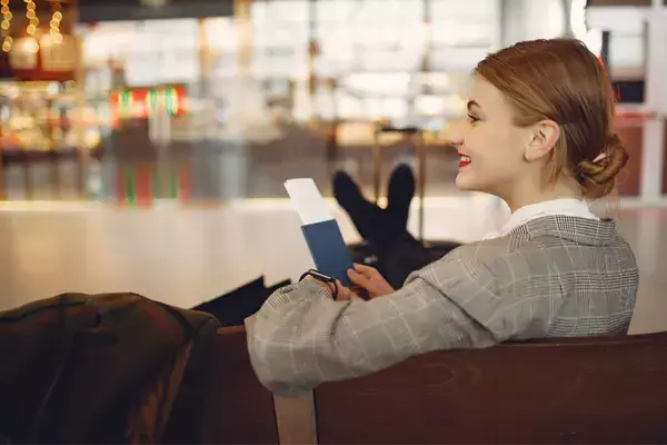 Moça em aeroporto sentada com passaporte na mão