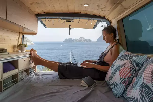 Mulher trabalhando em notebook em van na frente do mar