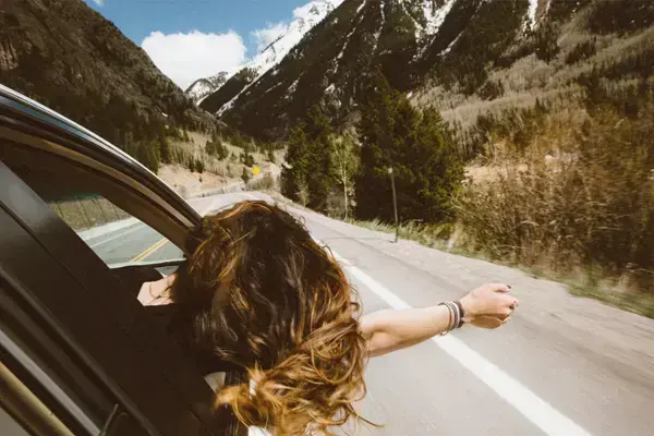 Mulher viajando, com braços para fora da janela do carro