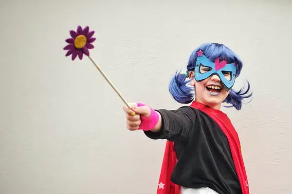 Criança fantasiada com cabelo azul, máscara e varinha com flor