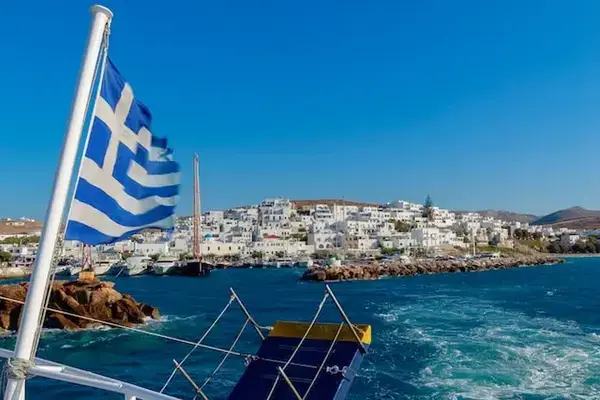 Barco com a bandeira da Grécia deixando a costa de Naoussa