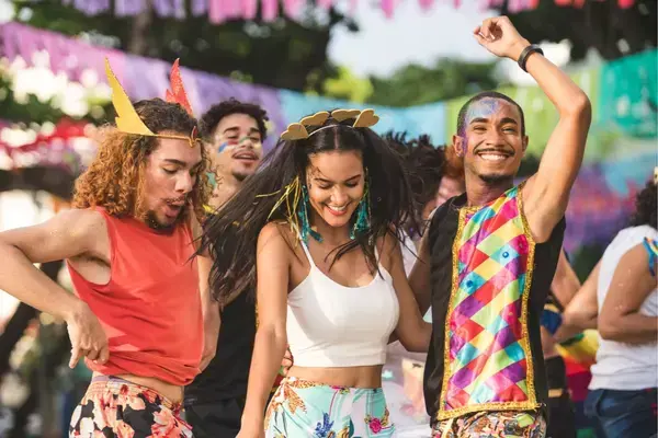 Pessoas com fantasias coloridas, brilhos e confetes curtindo o Carnaval com sorriso no rosto