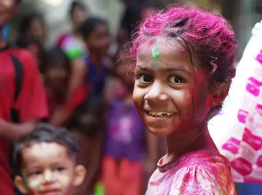Criança indiana sorrindo com pós coloridos no rosto durante o Holi Festival