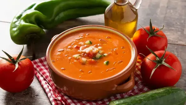 um prato com sopa na cor laranja em cima da mesa com tomates ao lado
