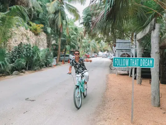 homem em bicicleta apontando para placa escrito "follow that dream!