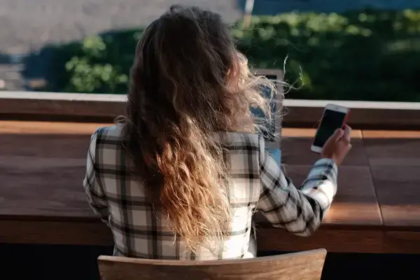 mulher com celular na mão e trabalhando no notebook em ambiente externo