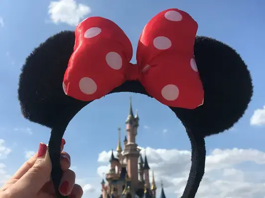 Pessoa segurando tiara da Minnie com castelo da Disney ao fundo