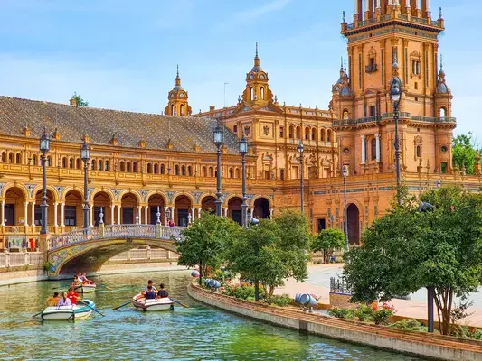 um grupo de pessoas no barquinho no rio em frente a um edifício bege e arvores em torno