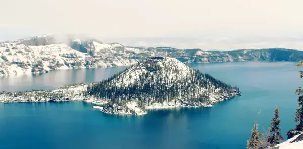 um lago cercado por arvores e montanhas sob o céu azul