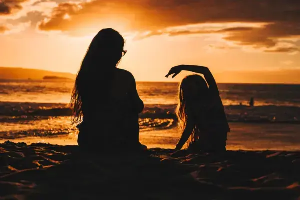 Mãe e filha na areia da praia no pôr do sol