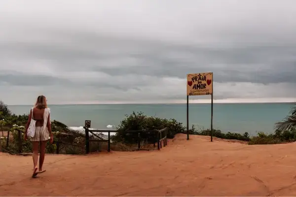 Emilly caminhando em frente a placa da Praia do Amor em Pipa, Rio Grande do Norte