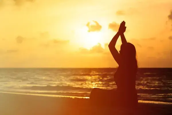 Silhueta de mulher meditando em praia no entardecer