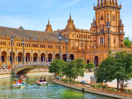 um grupo de pessoas no barquinho no rio em frente a um edifício bege e arvores em torno