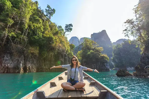 uma mulher no barco em um rio, ela está turistando feliz e fazendo pose com os braços abertos