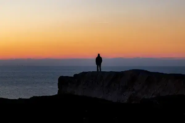 Homem contemplando o por do sol em rochas de uma praia