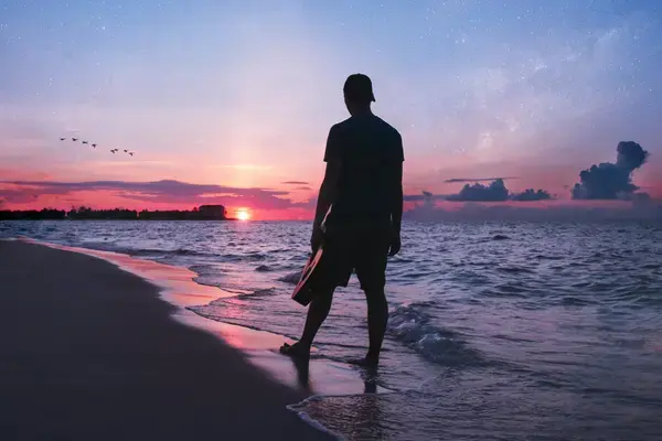homem de costa andando em direção ao mar durante o por do sol