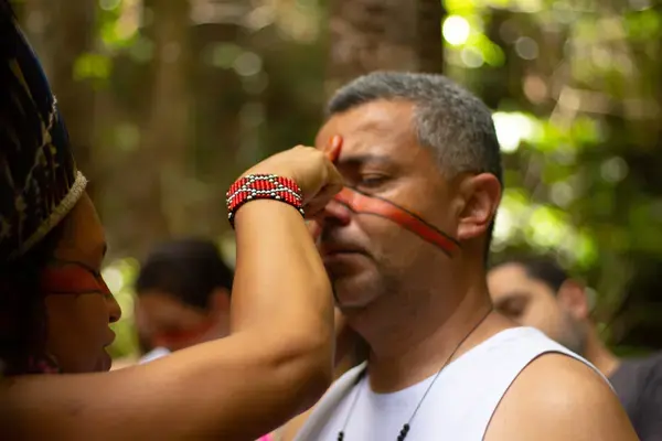 Pajé pintando rosto de homem durante ritual em experiência