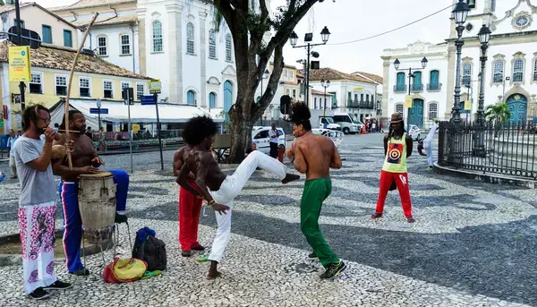 pessoas na praça praticando uma arte marcial conhecida como capoeira