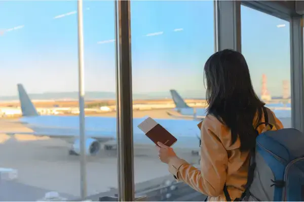 Mulher em aeroporto segurando um passaporte e olhando para avião