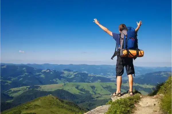Homem alegre, com uma mochila nas costas e em uma montanha
