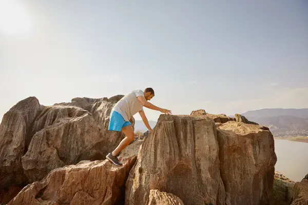 homem com deficiencia física usando bermuda azul escalando a montanha para a paisagem