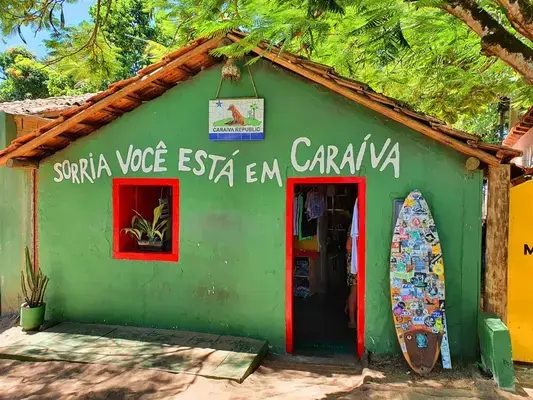 casa verde com detalhes colorido, uma árvore em volta e com um escrito na fachada da casa dizendo: sorria, você está em caraíva