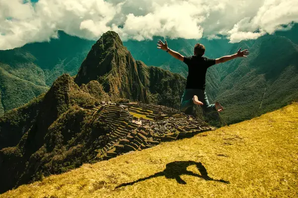 Homem pulando em frente as antigas construções de Machu Picchu