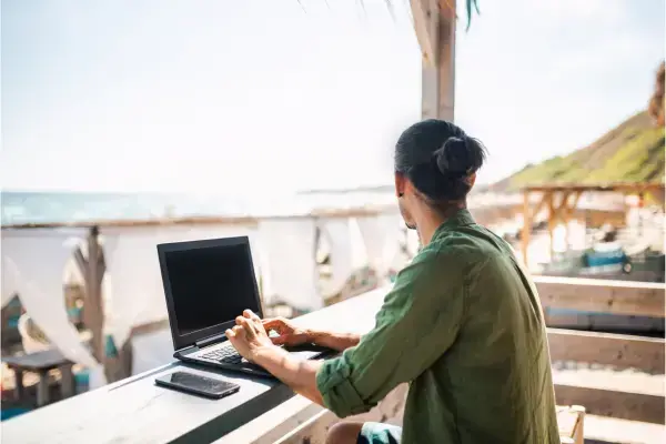 Homem trabalhando com notebook em restaurante ao lado de praia