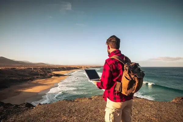 homem com um computador na mão na beira da praia