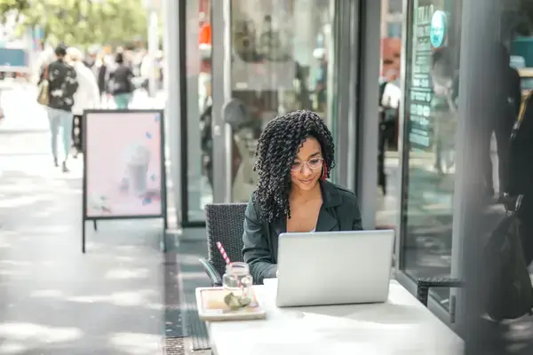 mulher-jovem-usando-laptop-enquanto-toma-uma-bebida-saborosa-em-um-cafe-de-rua-moderno