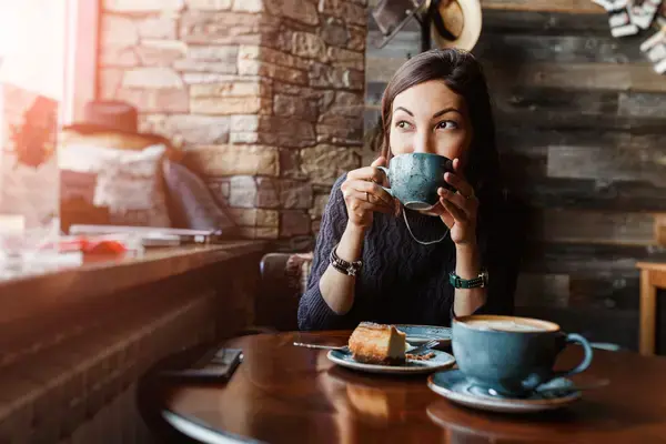 mulher levando uma xicara de café até a boca e sorrindo com os olhos