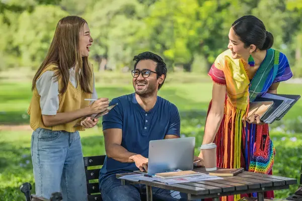 grupo de amigos rindo ao redor da mesa com computador e celular na mão