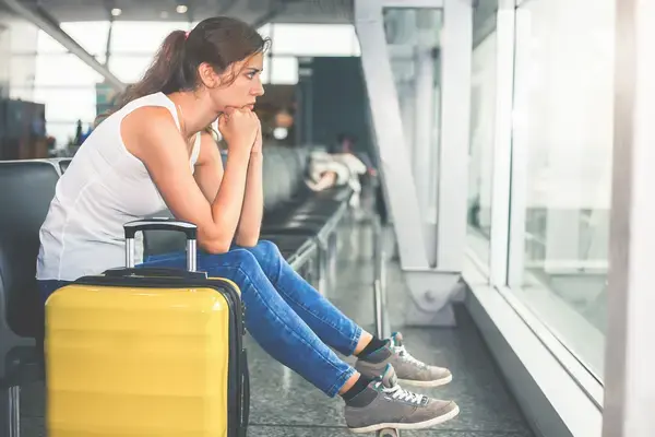 Mulher com expressão chateada esperando em aeroporto (Fonte: Adobe Stock)