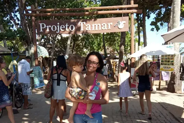 Mulher carregando criança em frente a placa do Projeto Tamar em Praia do Forte, Bahia Fonte: Arquivo Pessoal