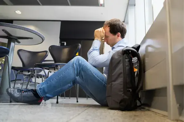 homem sentado no chão ao lado de uma mala no aeroporto