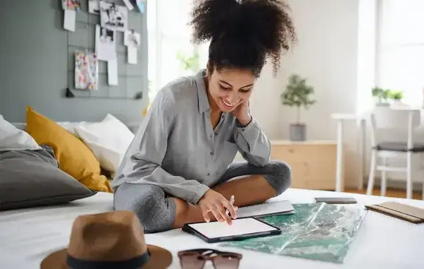 mulher negra sorrindo sentada em cima de uma cama planejando sua viagem
