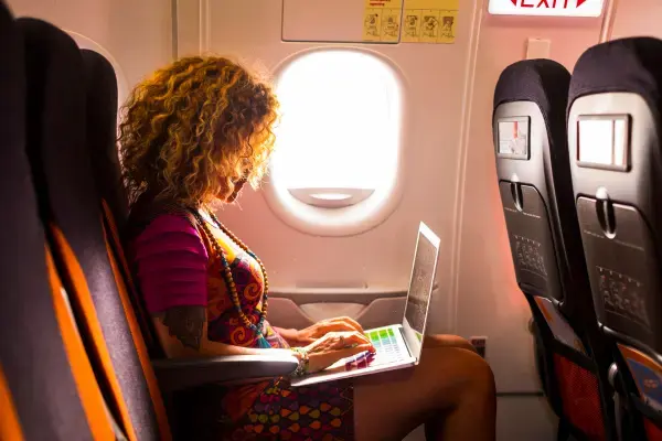 mulher sentada no banco de um avião. ela está mexendo no computador