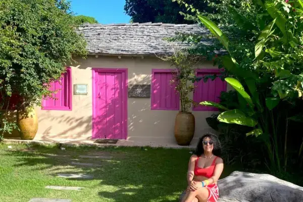 mulher sentada na pedra em frente a casa rosa