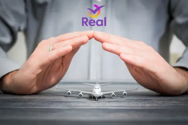 um par de mãos protegendo uma miniatura de avião, coma logo da Real Seguro Viagem logo acima