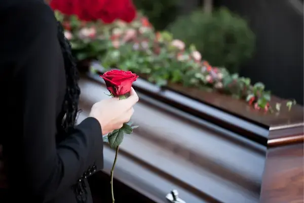 Mulher segurando rosa em frente a um caixão (Fonte: Canva)
