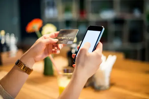Mãos de pessoa segurando um celular ao lado de cartão de crédito