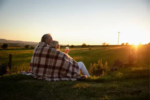 Casal enrolados em uma coberta, tomando vinho e olhando para por do sol