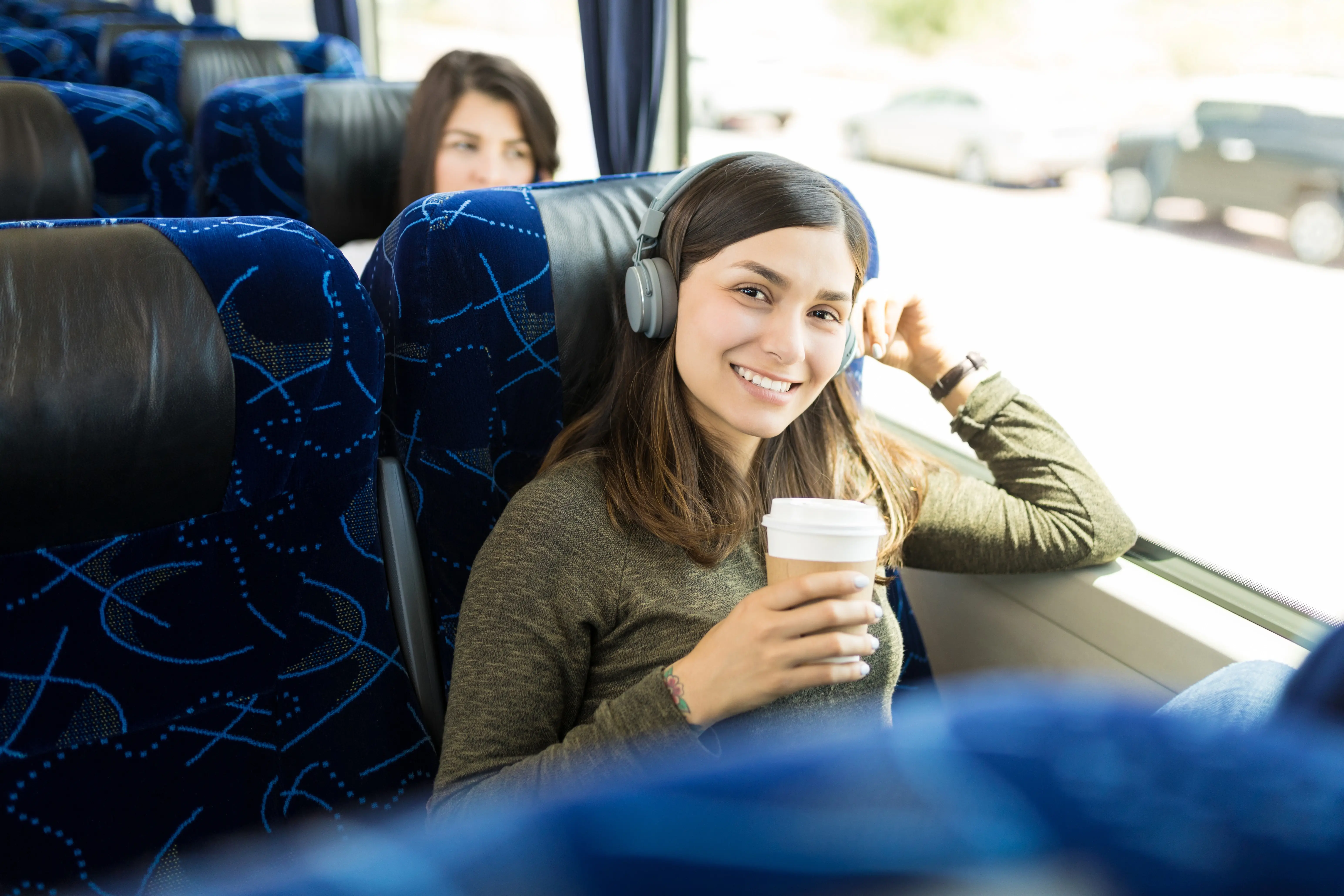 mulher sentada no banco do onibus segurando um copo de café e está com fones de ouvido