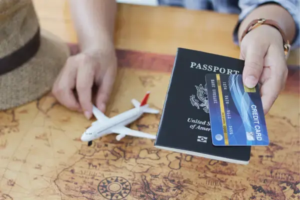 Pessoa segurando avião de brinquedo, passaporte e cartão de crédito (Fonte: Canva)