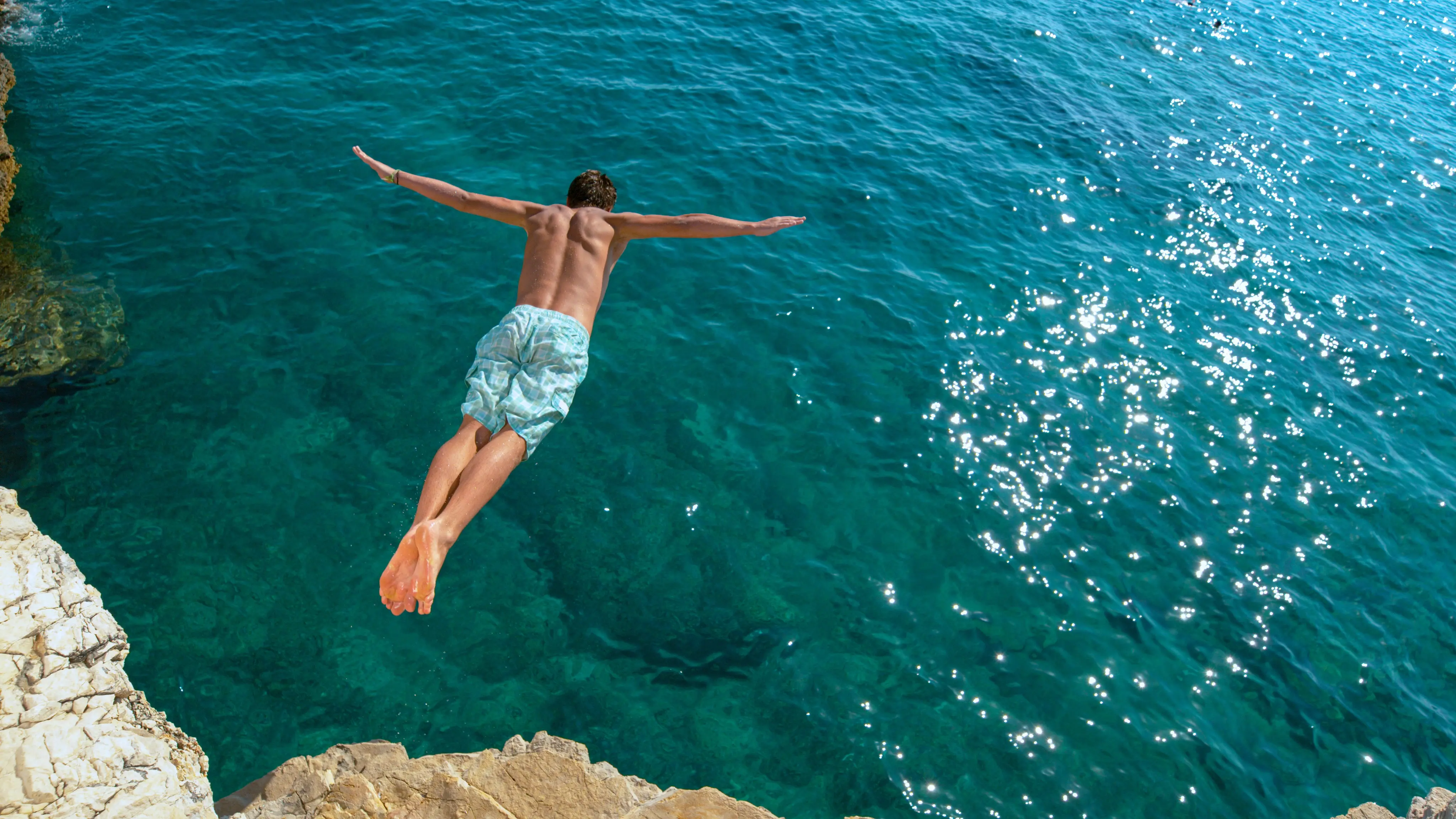 homem pulando no mar de águas cristalinas