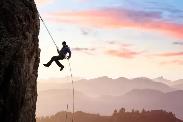 Homem fazendo canyoning, pendurado em uma corda escalando canion